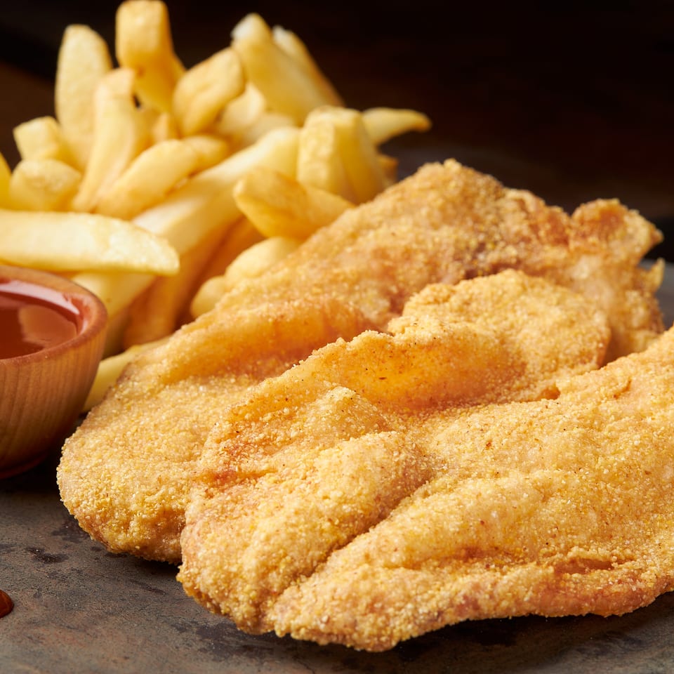 Golden breaded chicken tenders with French fries and dipping sauce arranged on a dark serving platter.