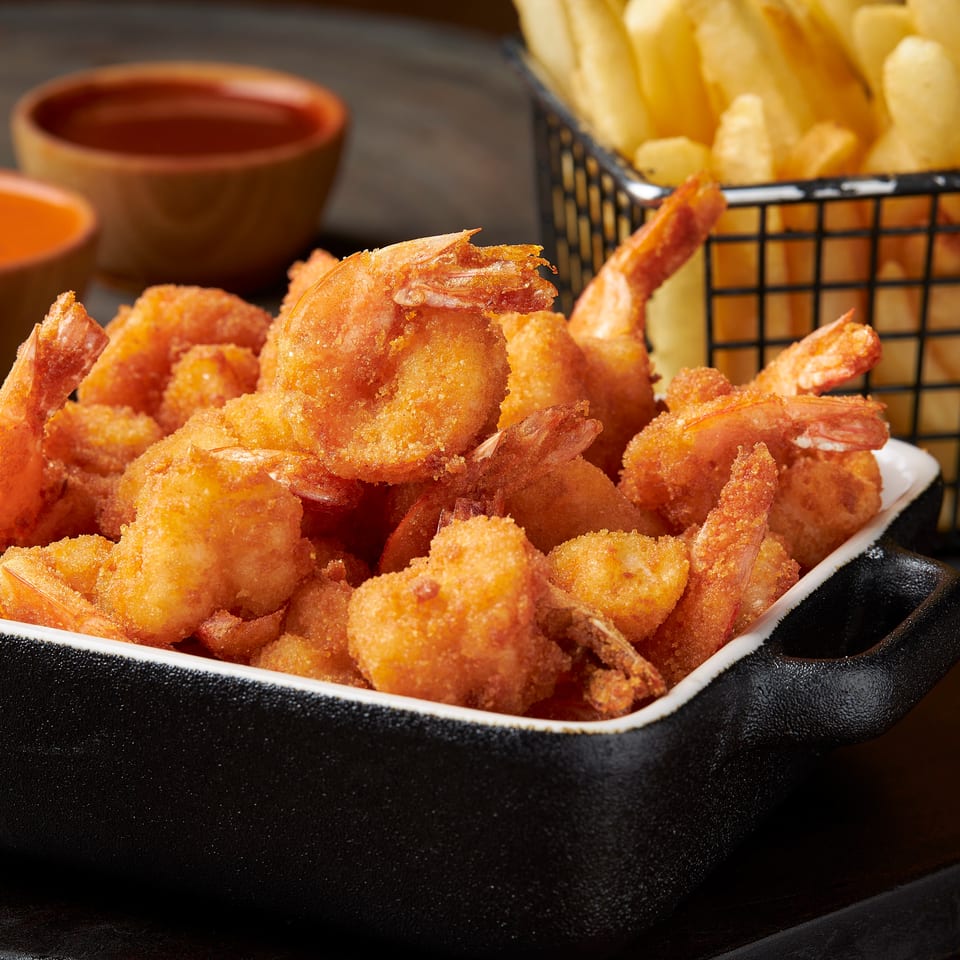 Crispy breaded shrimp served in a black dish with French fries and dipping sauces.