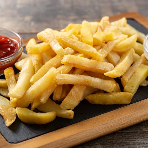 Golden french fries on a black serving board with ketchup and mayonnaise.