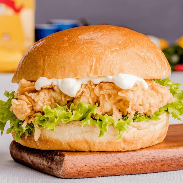Crispy chicken sandwich with lettuce and mayonnaise on a bun, on a wooden board.