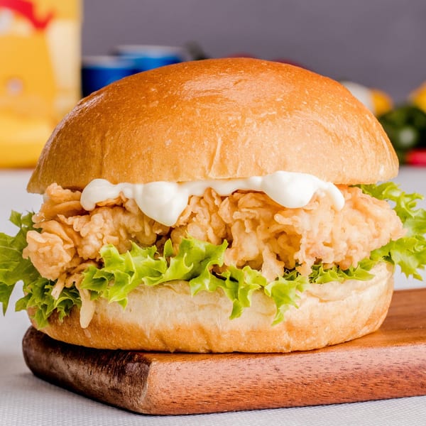 Crispy fried chicken sandwich with lettuce and mayonnaise on a bun, served on a wooden board.