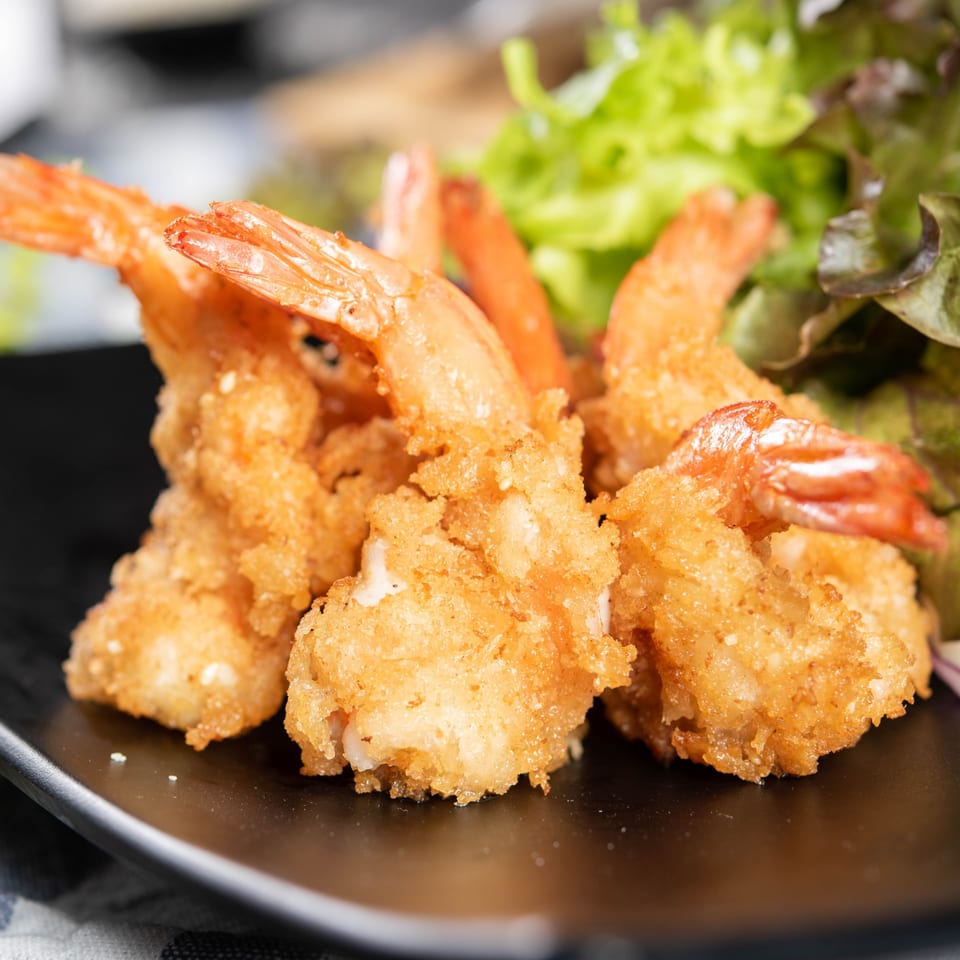 Close-up of crispy fried shrimp with tails on, served on a black plate with fresh green lettuce.