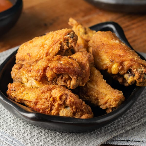 Crispy golden-brown fried chicken wings, seasoned and piled in a black bowl on a gray placemat.