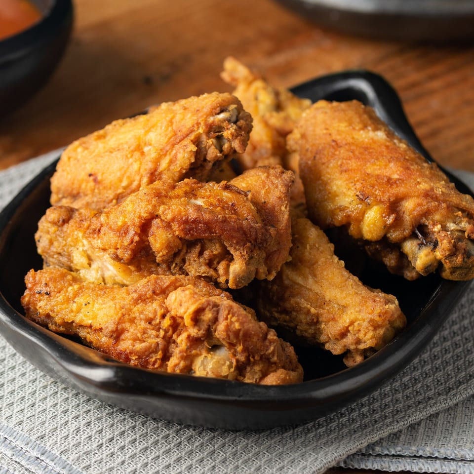 Crispy golden-brown fried chicken wings, seasoned and piled in a black bowl on a gray placemat.