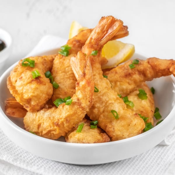 A white bowl filled with golden-brown fried shrimp, garnished with chopped green onions and lemon wedges.